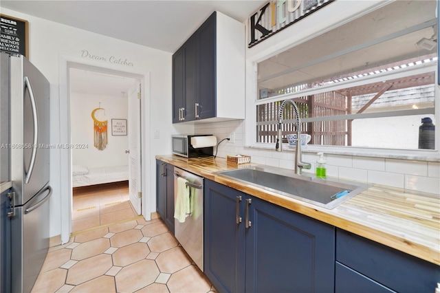 kitchen with sink, decorative backsplash, light tile patterned floors, butcher block countertops, and stainless steel appliances