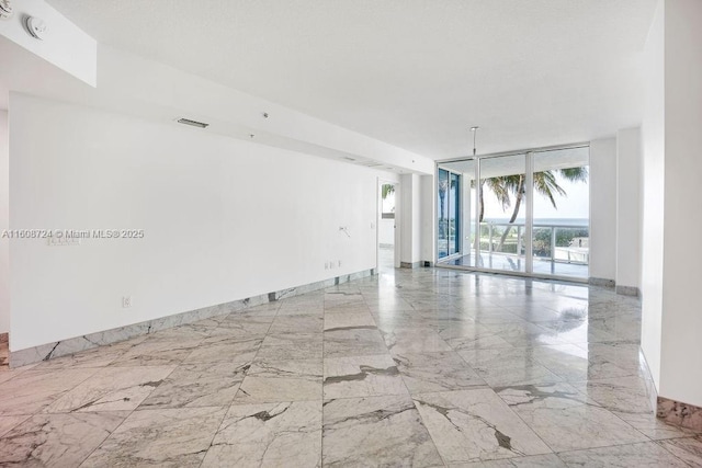 unfurnished room with marble finish floor, visible vents, baseboards, and a wall of windows