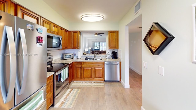 kitchen featuring sink, ceiling fan, stainless steel appliances, light stone countertops, and light wood-type flooring