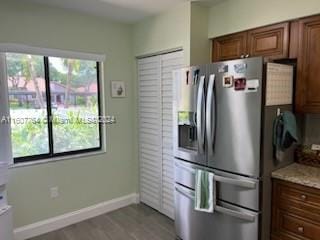 kitchen featuring light stone countertops, a healthy amount of sunlight, light wood-type flooring, and stainless steel fridge with ice dispenser