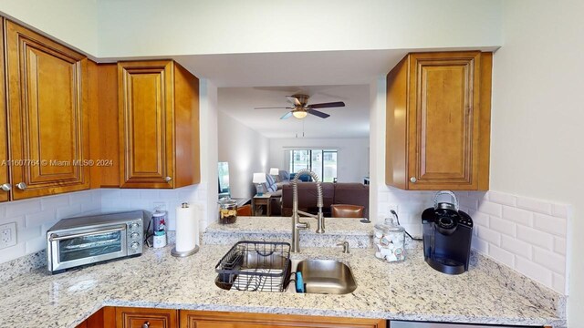 kitchen with light stone counters, ceiling fan, sink, and tasteful backsplash