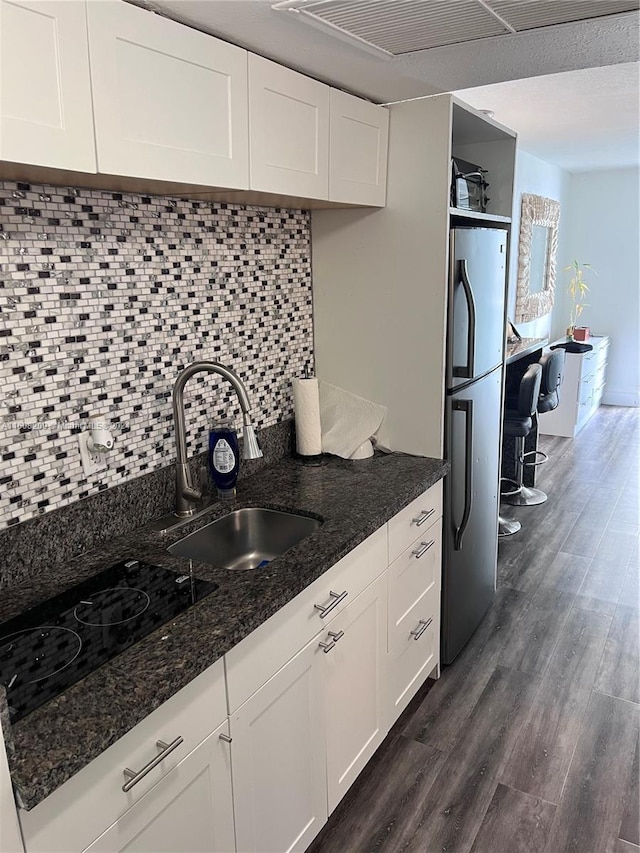 kitchen featuring dark wood-type flooring, dark stone counters, white cabinets, sink, and stainless steel refrigerator