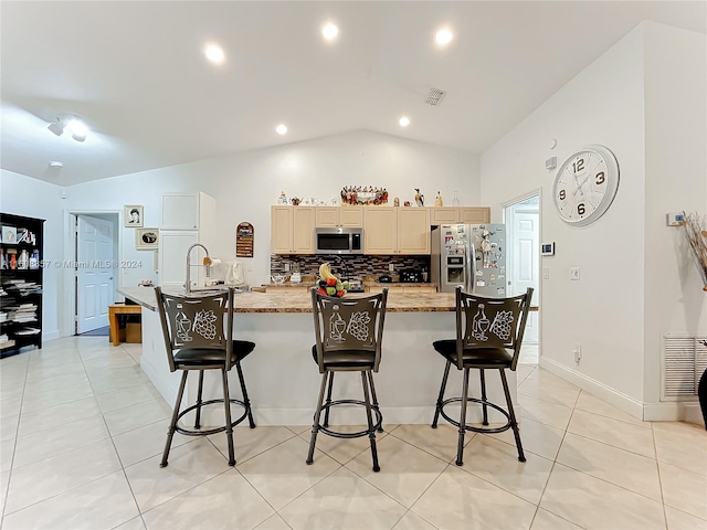 kitchen with backsplash, a breakfast bar area, an island with sink, appliances with stainless steel finishes, and lofted ceiling