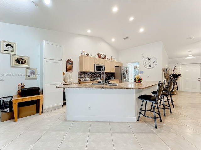 kitchen featuring a kitchen breakfast bar, tasteful backsplash, an island with sink, stainless steel appliances, and lofted ceiling