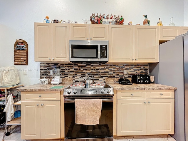 kitchen featuring stainless steel appliances, cream cabinetry, backsplash, and light tile floors