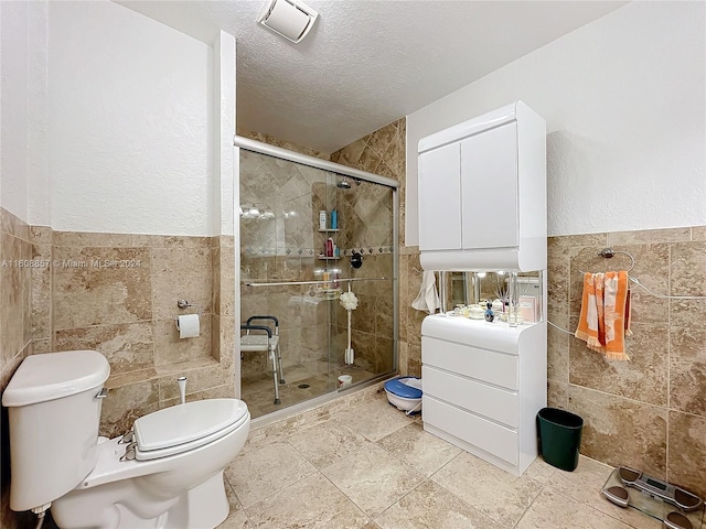 bathroom with tile walls, toilet, a textured ceiling, and a shower with door