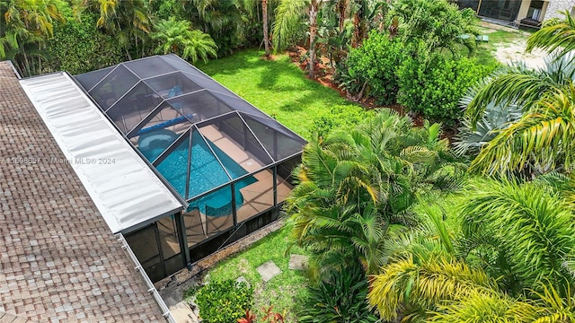 view of pool featuring glass enclosure and a lawn