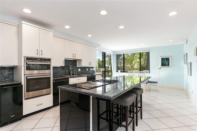 kitchen featuring a breakfast bar area, tasteful backsplash, light tile patterned floors, double oven, and black dishwasher