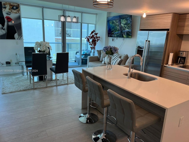 kitchen featuring a breakfast bar, a kitchen island with sink, sink, stainless steel fridge with ice dispenser, and light hardwood / wood-style floors