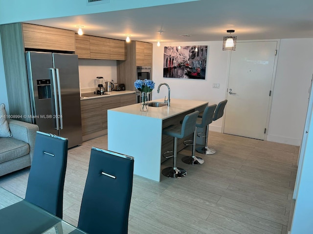 kitchen featuring a center island with sink, sink, black electric cooktop, a kitchen bar, and stainless steel fridge with ice dispenser