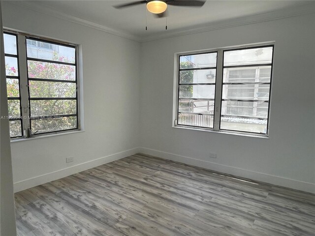 empty room with a wealth of natural light, wood-type flooring, ornamental molding, and ceiling fan