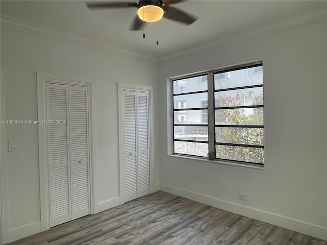 unfurnished bedroom featuring hardwood / wood-style floors, two closets, ceiling fan, and crown molding