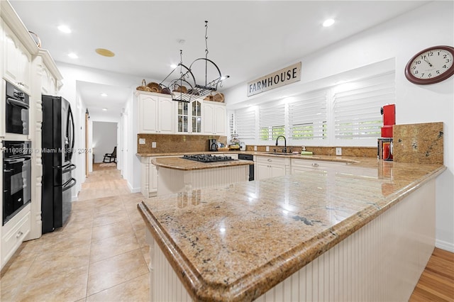 kitchen with kitchen peninsula, light stone counters, sink, black appliances, and a kitchen island