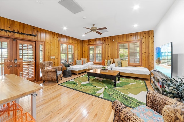 living room featuring ceiling fan, light hardwood / wood-style floors, wooden walls, and french doors