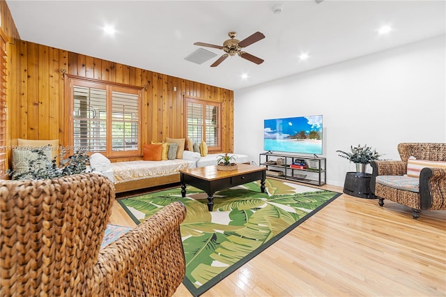 living room with ceiling fan, wood walls, and wood-type flooring