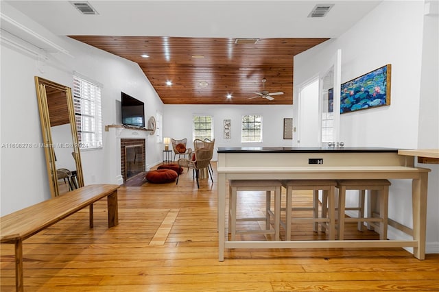 interior space featuring ceiling fan, light hardwood / wood-style flooring, vaulted ceiling, a fireplace, and wood ceiling