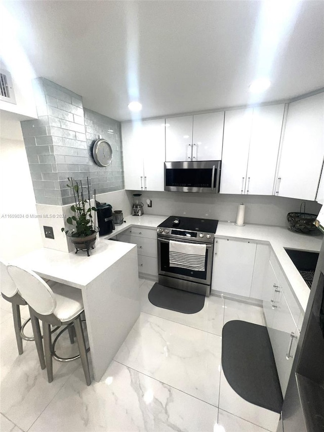 kitchen with white cabinetry, stainless steel appliances, backsplash, kitchen peninsula, and a breakfast bar area