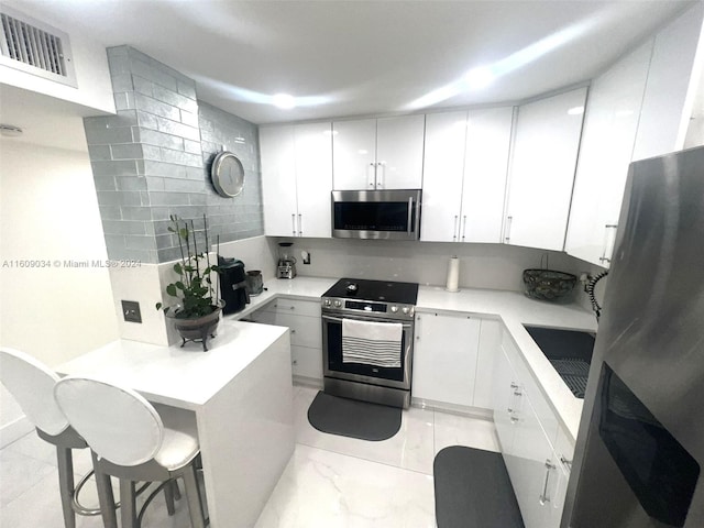 kitchen with white cabinets, appliances with stainless steel finishes, decorative backsplash, and a kitchen breakfast bar