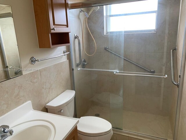 bathroom featuring tile walls, a shower with shower door, vanity, and toilet