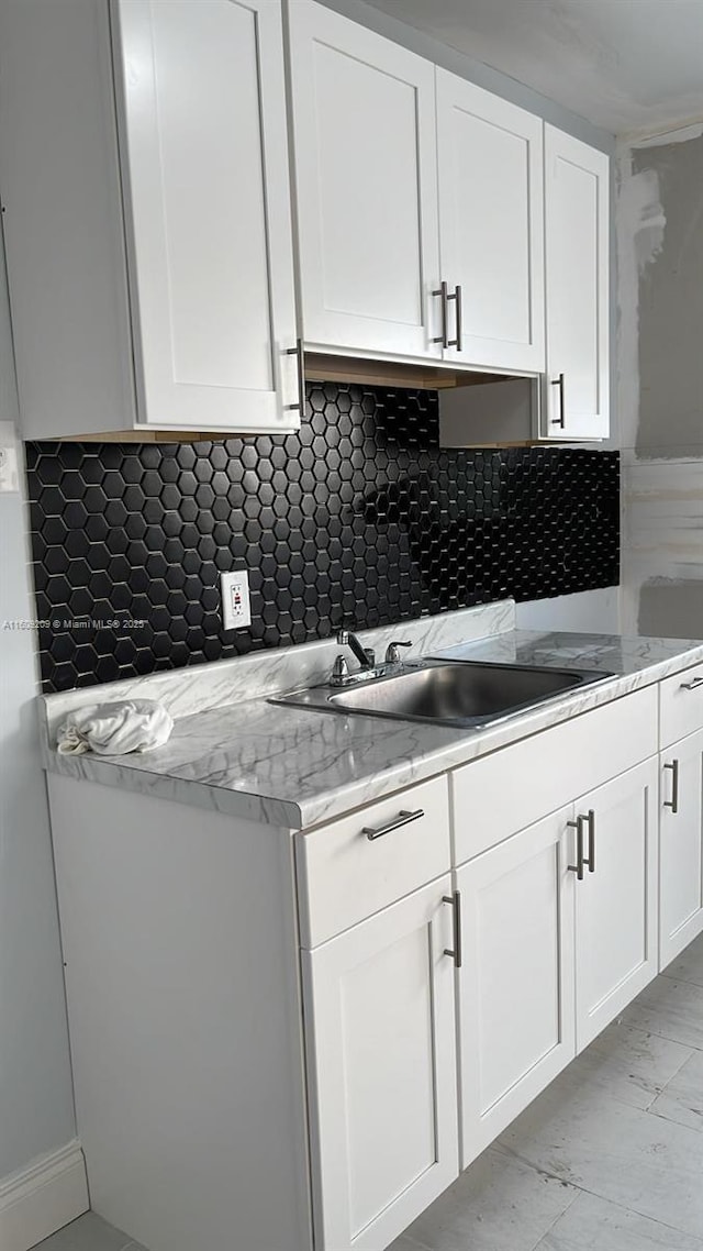 kitchen featuring light stone counters, sink, decorative backsplash, and white cabinets