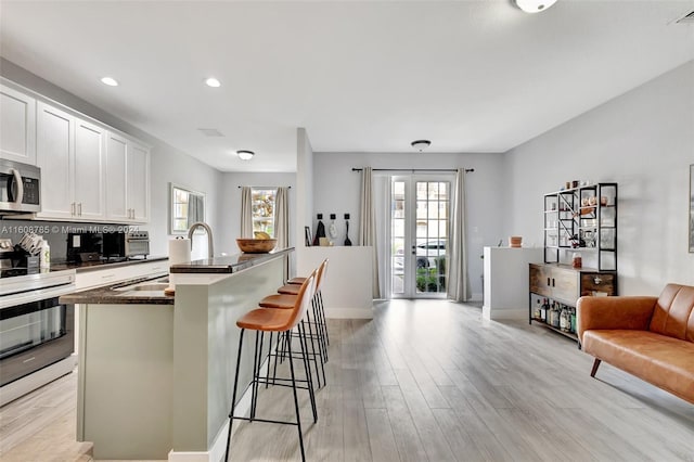 kitchen with white cabinets, a kitchen bar, stainless steel appliances, sink, and a kitchen island with sink