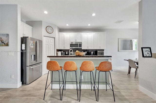 kitchen with white cabinetry, an island with sink, stainless steel appliances, tasteful backsplash, and sink