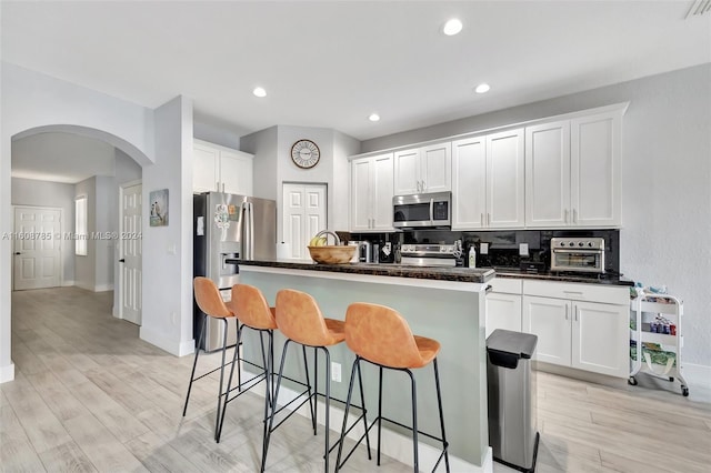 kitchen featuring white cabinets, a kitchen island with sink, stainless steel appliances, and a kitchen bar