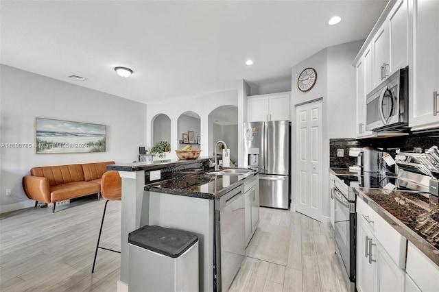 kitchen with white cabinets, appliances with stainless steel finishes, an island with sink, a kitchen breakfast bar, and sink