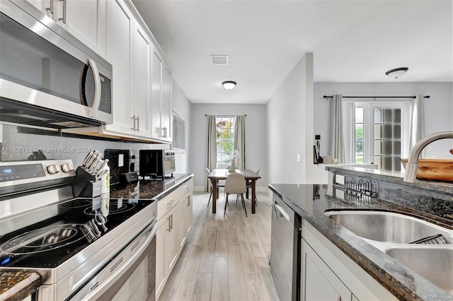 kitchen featuring white cabinetry, appliances with stainless steel finishes, plenty of natural light, dark stone countertops, and sink