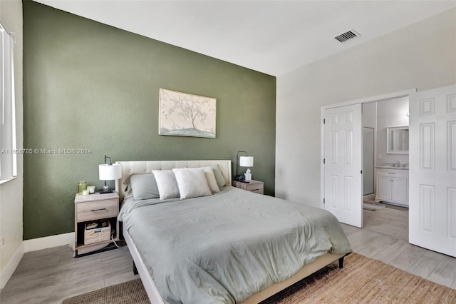 bedroom with ensuite bath, sink, and light hardwood / wood-style flooring