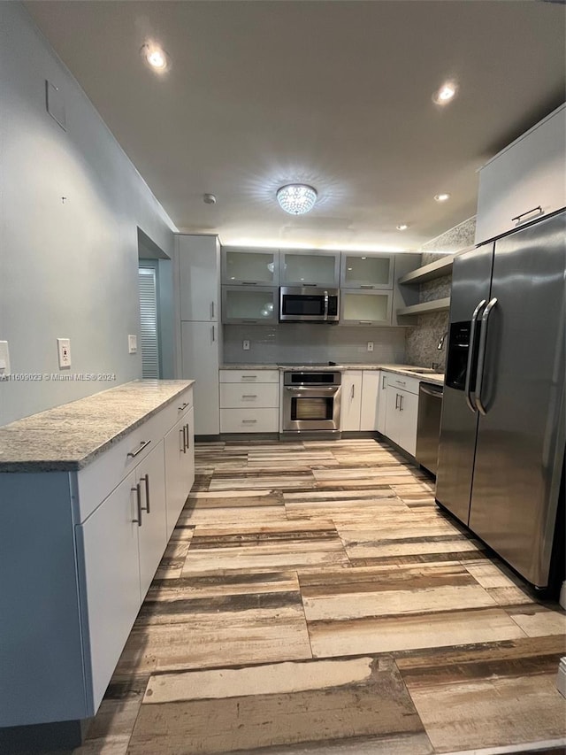 kitchen with light hardwood / wood-style floors, sink, backsplash, white cabinets, and appliances with stainless steel finishes