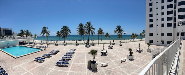 view of pool with a water view, a view of the beach, and a patio area