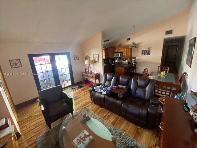 living room featuring light hardwood / wood-style floors, french doors, and vaulted ceiling