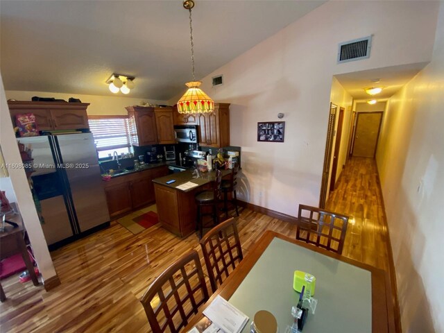 kitchen with sink, lofted ceiling, decorative light fixtures, appliances with stainless steel finishes, and light wood-type flooring