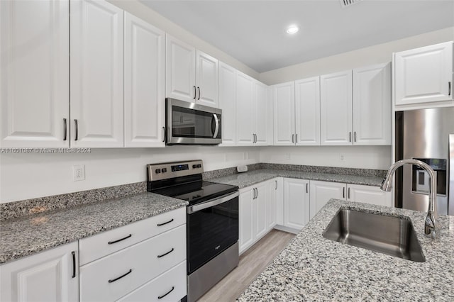 kitchen with light stone countertops, white cabinets, stainless steel appliances, sink, and light wood-type flooring