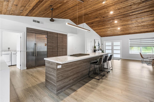 kitchen with wood ceiling, independent washer and dryer, vaulted ceiling, a kitchen island, and stainless steel built in refrigerator