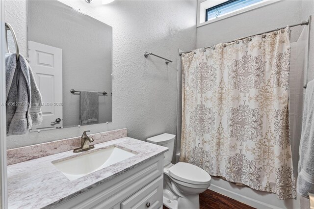 full bathroom featuring hardwood / wood-style flooring, shower / tub combo with curtain, vanity, and toilet