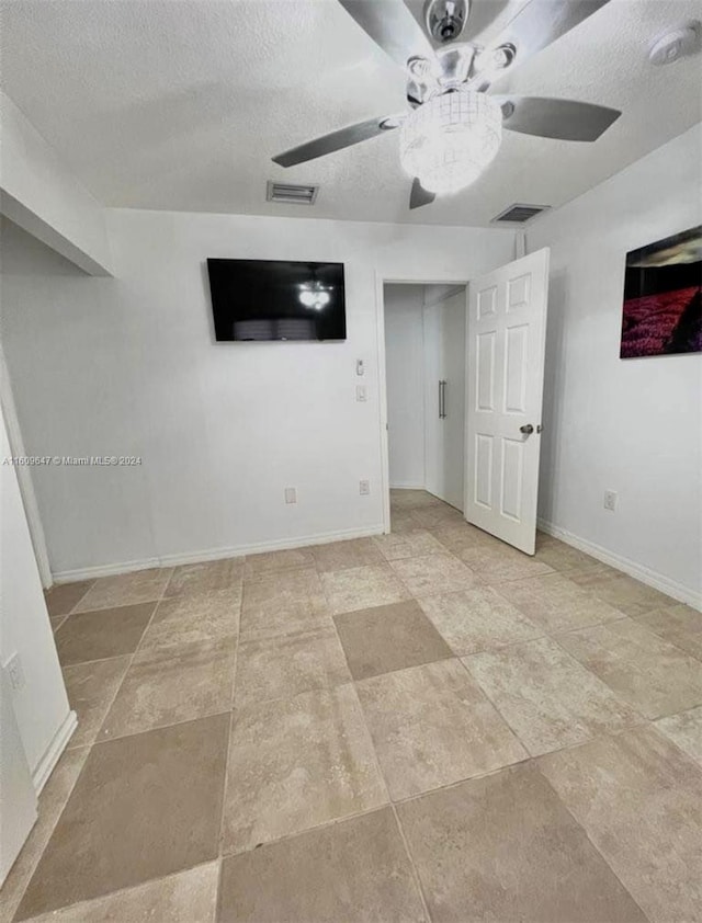 tiled spare room featuring a textured ceiling and ceiling fan