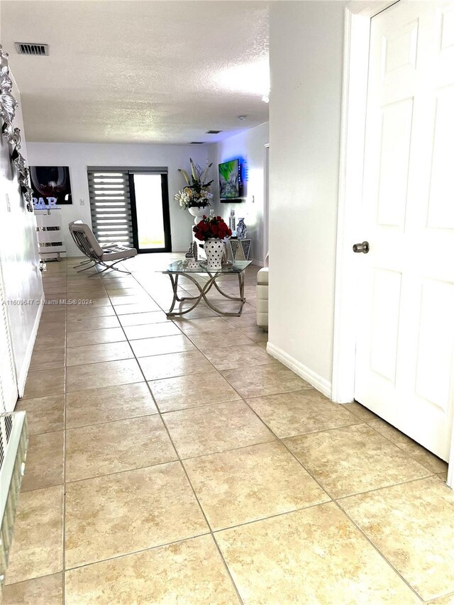 hallway with a textured ceiling and light tile patterned floors