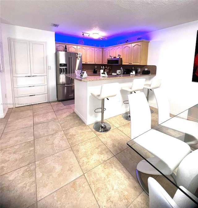 kitchen with light tile patterned flooring, stainless steel appliances, a kitchen bar, and kitchen peninsula