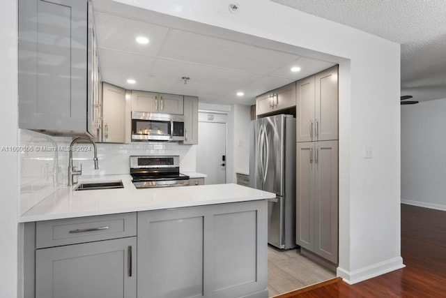 kitchen with sink, kitchen peninsula, gray cabinetry, stainless steel appliances, and hardwood / wood-style floors