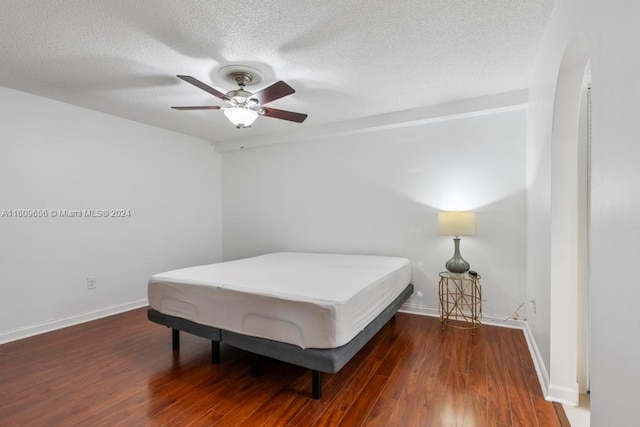 bedroom with ceiling fan, a textured ceiling, and dark hardwood / wood-style floors