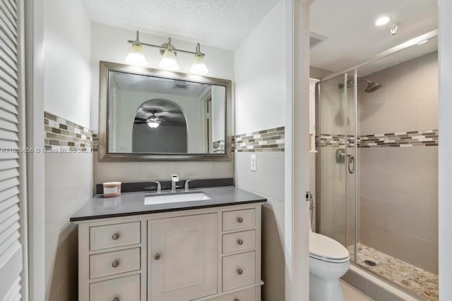 bathroom with tile walls, a textured ceiling, a shower with shower door, vanity, and toilet