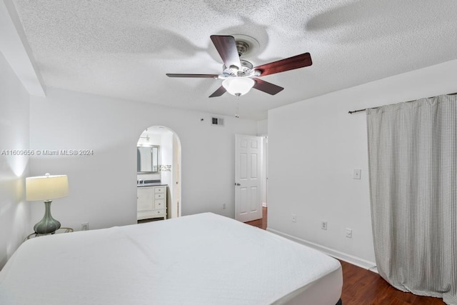 bedroom with ceiling fan, a textured ceiling, connected bathroom, and dark wood-type flooring