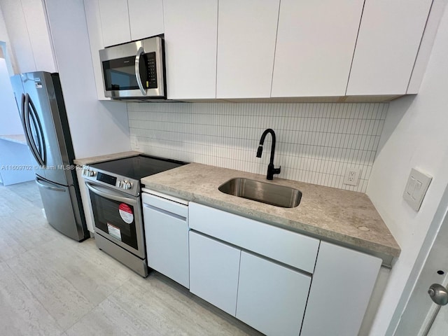 kitchen with appliances with stainless steel finishes, white cabinets, sink, and tasteful backsplash