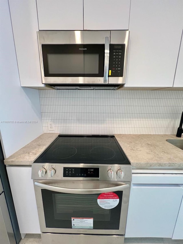 kitchen with backsplash, appliances with stainless steel finishes, and white cabinets