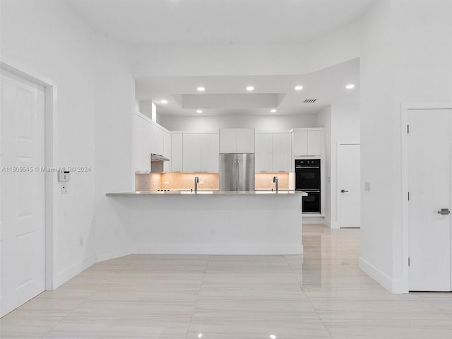 kitchen featuring tasteful backsplash, high end fridge, a raised ceiling, light tile floors, and white cabinetry