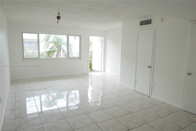 spare room with a textured ceiling, plenty of natural light, and light tile floors