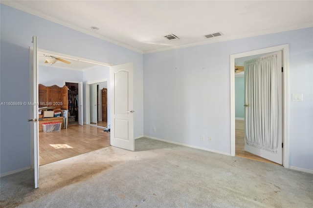 unfurnished bedroom featuring carpet floors, a walk in closet, visible vents, and crown molding