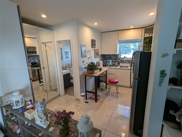 kitchen featuring tasteful backsplash, fridge, stainless steel microwave, light tile floors, and white cabinetry